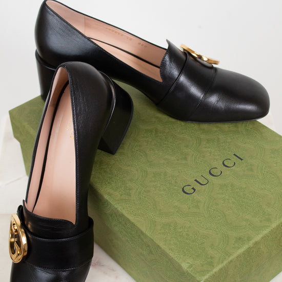 Black leather loafers with gold hardware details displayed on top of green 'GUCCI' box against a plain background