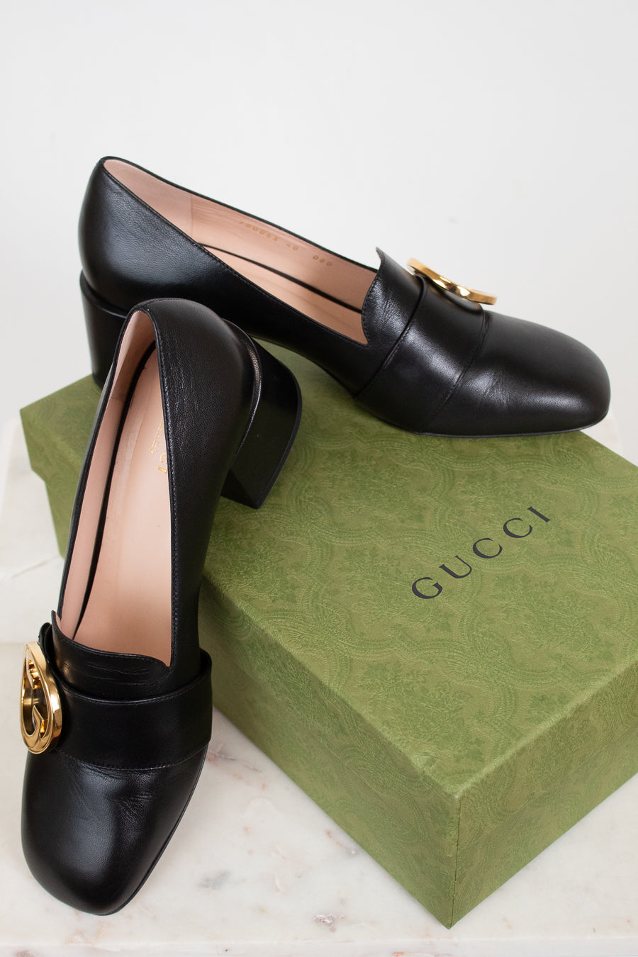 Black leather loafers with gold hardware details displayed on top of green 'GUCCI' box against a plain background