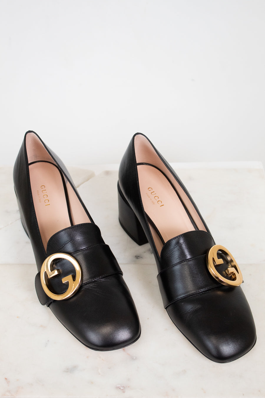 Black leather heeled loafers with gold 'GG' against a marble plain background