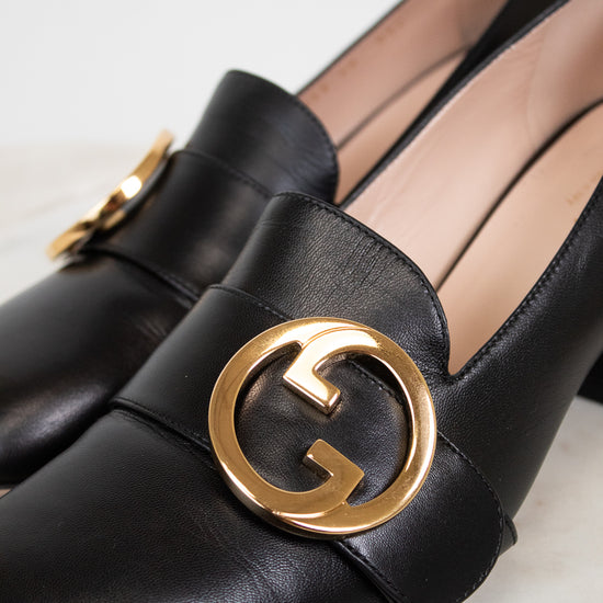 Close up of gold 'GG' hardware logo detail on black leather loafers