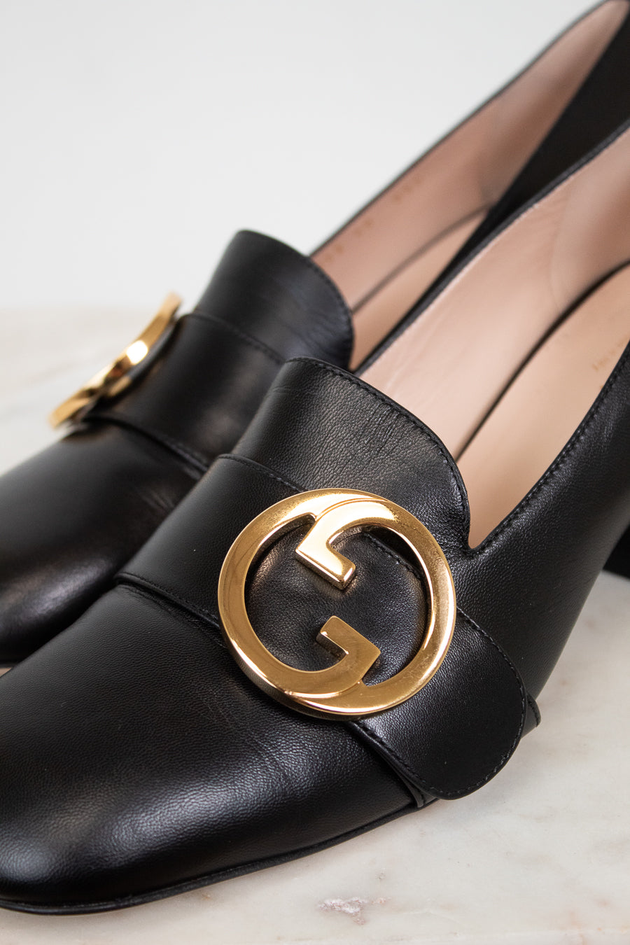 Close up of gold 'GG' hardware logo detail on black leather loafers