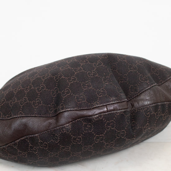 A dark brown Gucci monogram canvas and leather bag or pouch, photographed on a light marble surface against a white background.