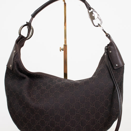 A dark brown Gucci hobo shoulder bag with the classic GG monogram canvas, displayed on a gold stand against a white background.