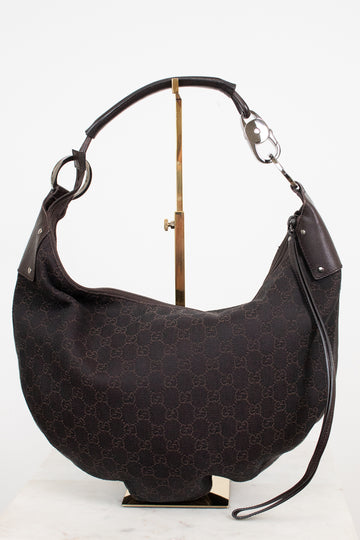 A dark brown Gucci hobo shoulder bag with the classic GG monogram canvas, displayed on a gold stand against a white background.