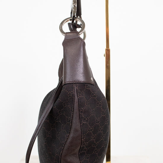 A dark brown Gucci shoulder bag with the brand's signature GG monogram canvas and leather trim, displayed on a gold metal stand against a white background.