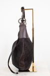 A dark brown Gucci shoulder bag with the brand's signature GG monogram canvas and leather trim, displayed on a gold metal stand against a white background.