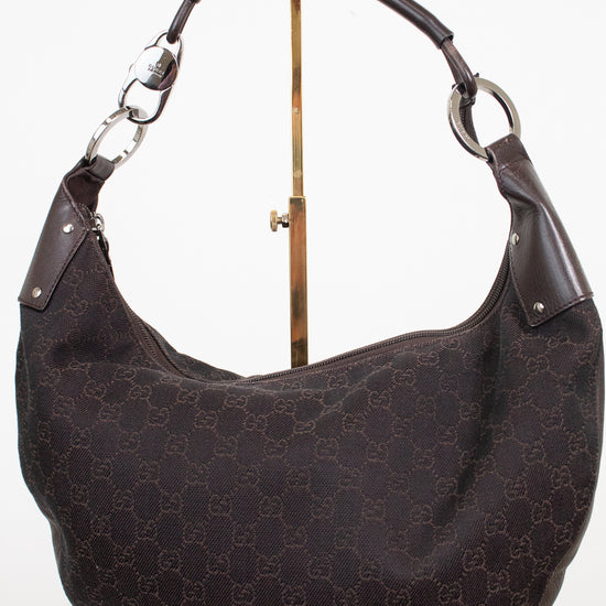 A dark brown Gucci hobo shoulder bag with the classic GG monogram canvas and dark brown leather trim, displayed on a stand against a white background.