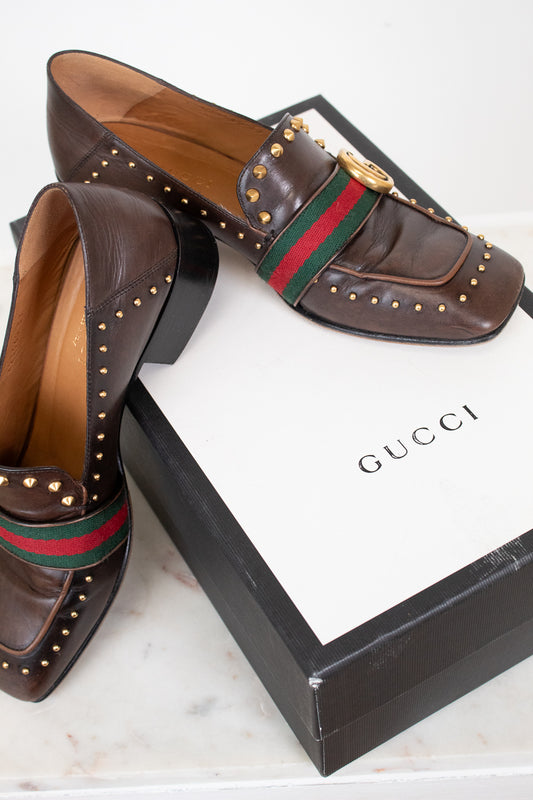 Brown Gucci loafers with studded details on a white box