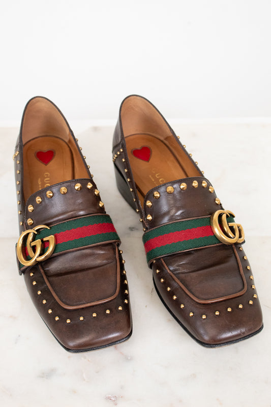 Brown leather loafers with gold studs and Gucci logo on a white background