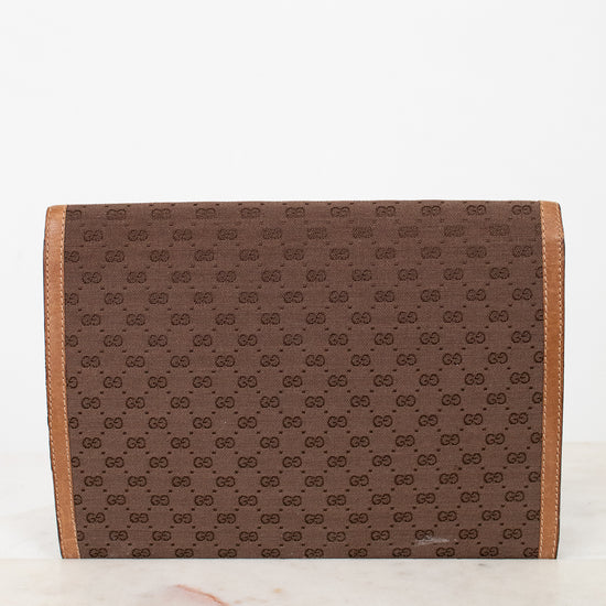 Brown Gucci monogram clutch purse with faint scratch on a white marble surface