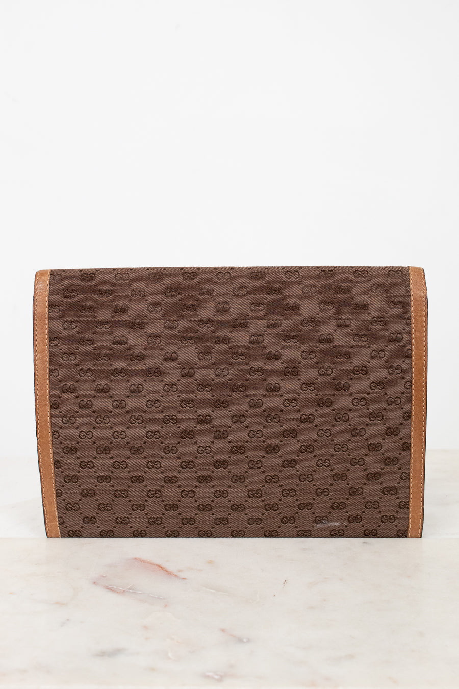 Brown Gucci monogram clutch purse with faint scratch on a white marble surface