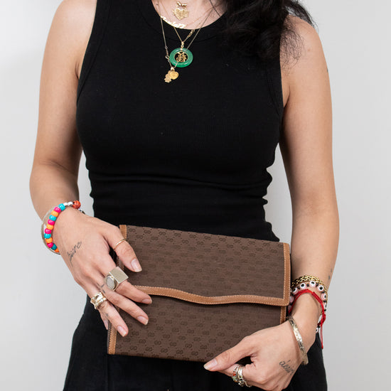 Person dressed in black holding brown Gucci monogram clutch purse with a white background