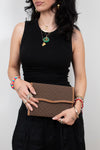 Person dressed in black holding brown Gucci monogram clutch purse with a white background