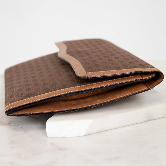 Side view of brown Gucci monogram clutch purse on a white marble surface