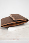 Side view of brown Gucci monogram clutch purse on a white marble surface