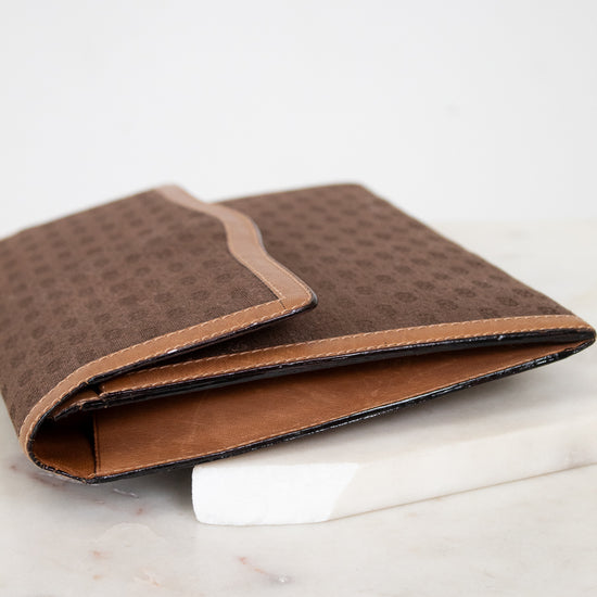 Side view of brown Gucci monogram clutch purse on a white marble surface