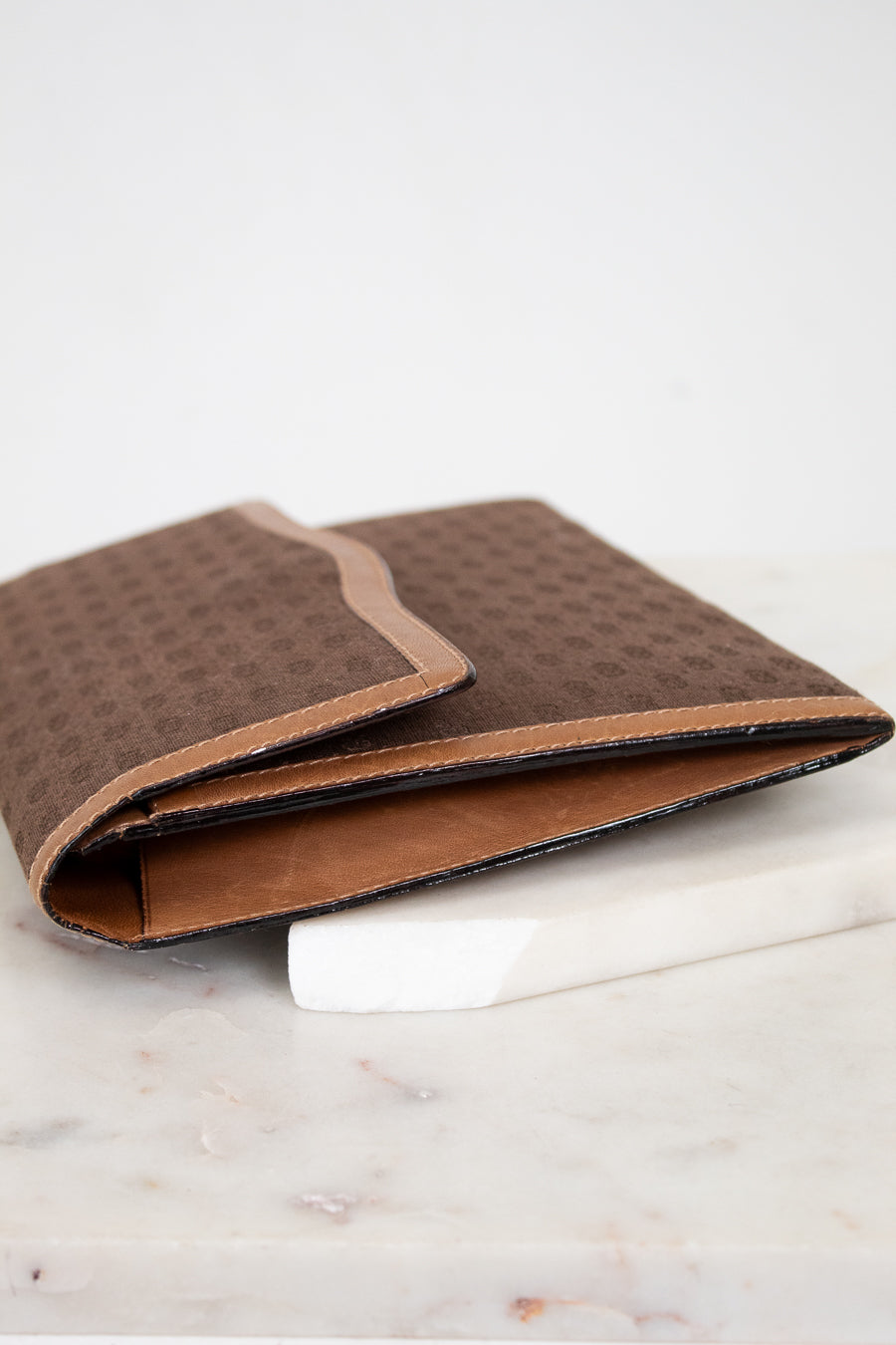 Side view of brown Gucci monogram clutch purse on a white marble surface