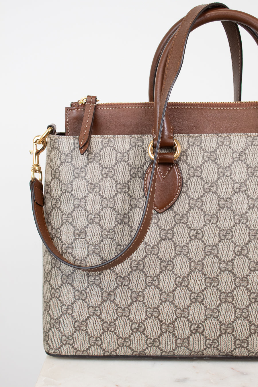 Gucci monogram canvas handbag with brown leather trim and handles, gold-tone hardware, and a detachable shoulder strap, shown on a clean white background.