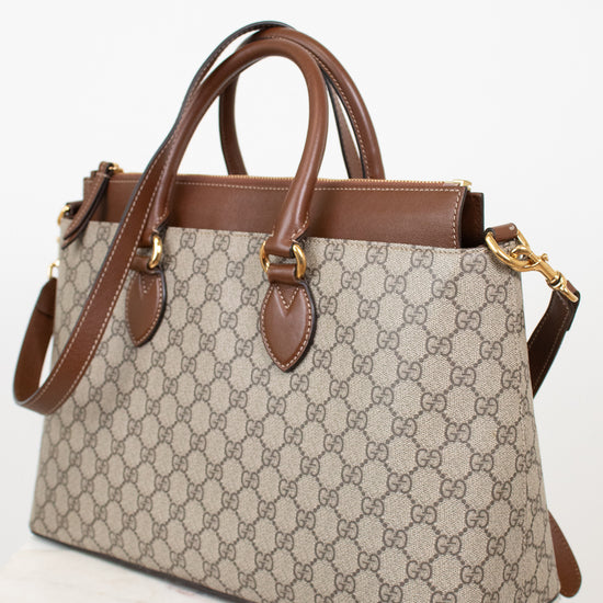 A Gucci GG Supreme handbag in beige and brown canvas with brown leather handles and trim, shown on a white marble surface against a white background.