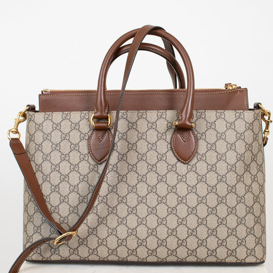 A Gucci monogram canvas handbag with brown leather handles and trim, displayed on a white marble block against a white background.