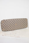 A Gucci shoulder bag in beige and brown GG Supreme canvas with gold-tone studs, resting on a white marble surface against a white background.