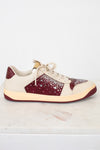A low-top sneaker with cream-colored panels, burgundy overlays, and a sparkling rhinestone-embellished side panel, resting on a white marble surface against a white background.