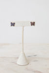 Pair of silver-tone GUCCI butterfly-shaped stud earrings with engraved logo detailing. Resting on a beige earring stand on a marble and white background.