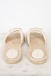 A pair of Gucci espadrille-style slide sandals with woven beige jute soles and white straps embellished with small rhinestones, shown on a light marble surface against a white background.