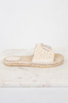 A single beige crochet espadrille-style slide sandal with a rhinestone-embellished strap, resting on a white marble slab against a white background.