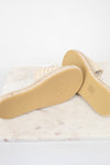 A pair of woven espadrille-style slide sandals shown from the sole side, resting on a white marble slab against a white background.