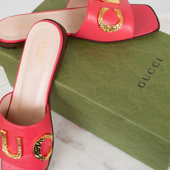 A pair of Gucci pink leather slide sandals with gold-tone horsebit hardware, displayed on top of a green Gucci shoebox on a white marble surface.