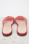A pair of pink leather Gucci flat slide sandals, with gold-tone letter detailing across the strap, and a dark brown sole, shown from the back on a light marble surface.