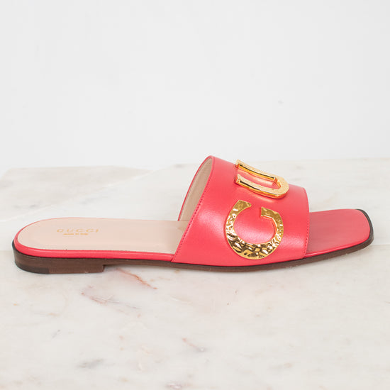 A single red leather slide sandal with gold-tone decorative hardware, displayed on a white marble surface against a white background.