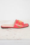 A single red leather slide sandal with gold-tone decorative hardware, displayed on a white marble surface against a white background.