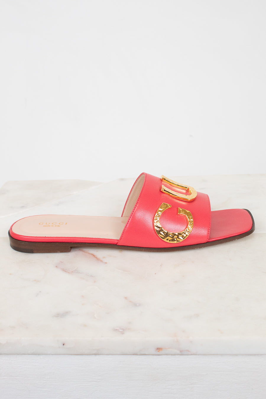 A single red leather slide sandal with gold-tone decorative hardware, displayed on a white marble surface against a white background.