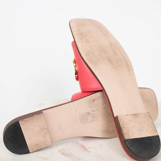 A pair of red leather flat sandals shown from the sole, resting on a white marble surface against a white background.