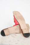 A pair of red leather flat sandals shown from the sole, resting on a white marble surface against a white background.
