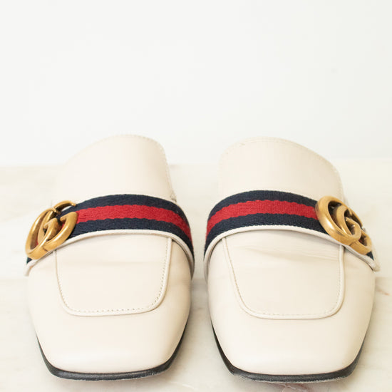 A pair of Gucci square-toe leather loafers in off-white, featuring the signature red and navy green web stripe across the top with a gold-tone interlocking GG logo on each side.