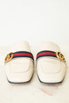 A pair of Gucci square-toe leather loafers in off-white, featuring the signature red and navy green web stripe across the top with a gold-tone interlocking GG logo on each side.