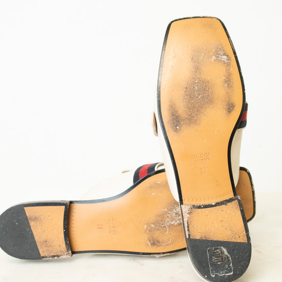 A pair of Gucci flat sandals shown from the sole, displaying the tan leather insoles with heavy scuffing and dirt, black rubber outsoles, and the signature red and green web stripe detail near the heel.