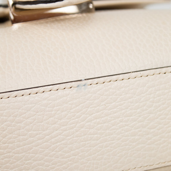 Close-up of a cream-colored pebbled leather handbag with a polished gold-tone metal ring handle and matching stitching.