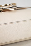 Close-up of a cream-colored pebbled leather handbag with a polished gold-tone metal ring handle and matching stitching.