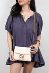 A woman wearing a dark purple puff-sleeve blouse and holding a cream-colored Gucci shoulder bag with a gold-tone horsebit logo clasp and chain strap, set against a plain light gray background.