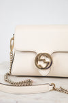 An off-white leather shoulder bag with a gold-tone interlocking G logo clasp and a matching chain strap, resting on a light marble surface.