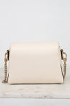 A cream-colored pebbled leather crossbody bag with a gold-tone chain strap, displayed on a white marble surface against a white background.