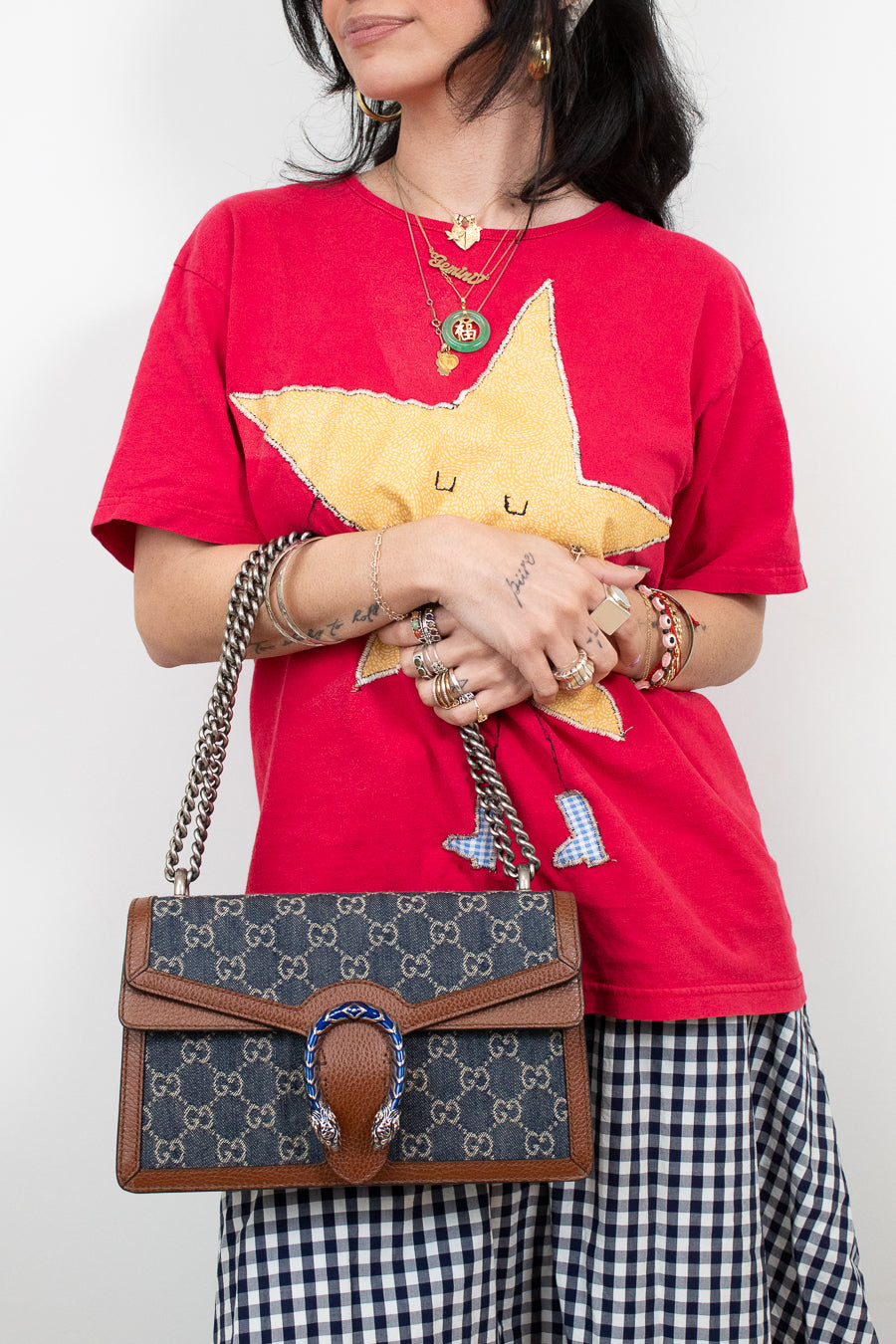 Person wearing a red shirt with a yellow star design, holding a Gucci handbag.