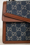 Close-up of a blue fabric bag with brown leather trim featuring a "GG" pattern.