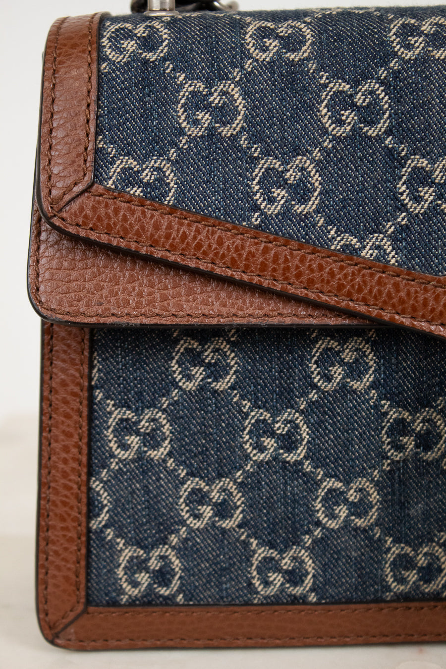 Close-up of a blue fabric bag with brown leather trim featuring a "GG" pattern.
