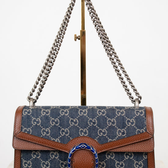 Designer handbag with silver chain strap on a stand against a white background