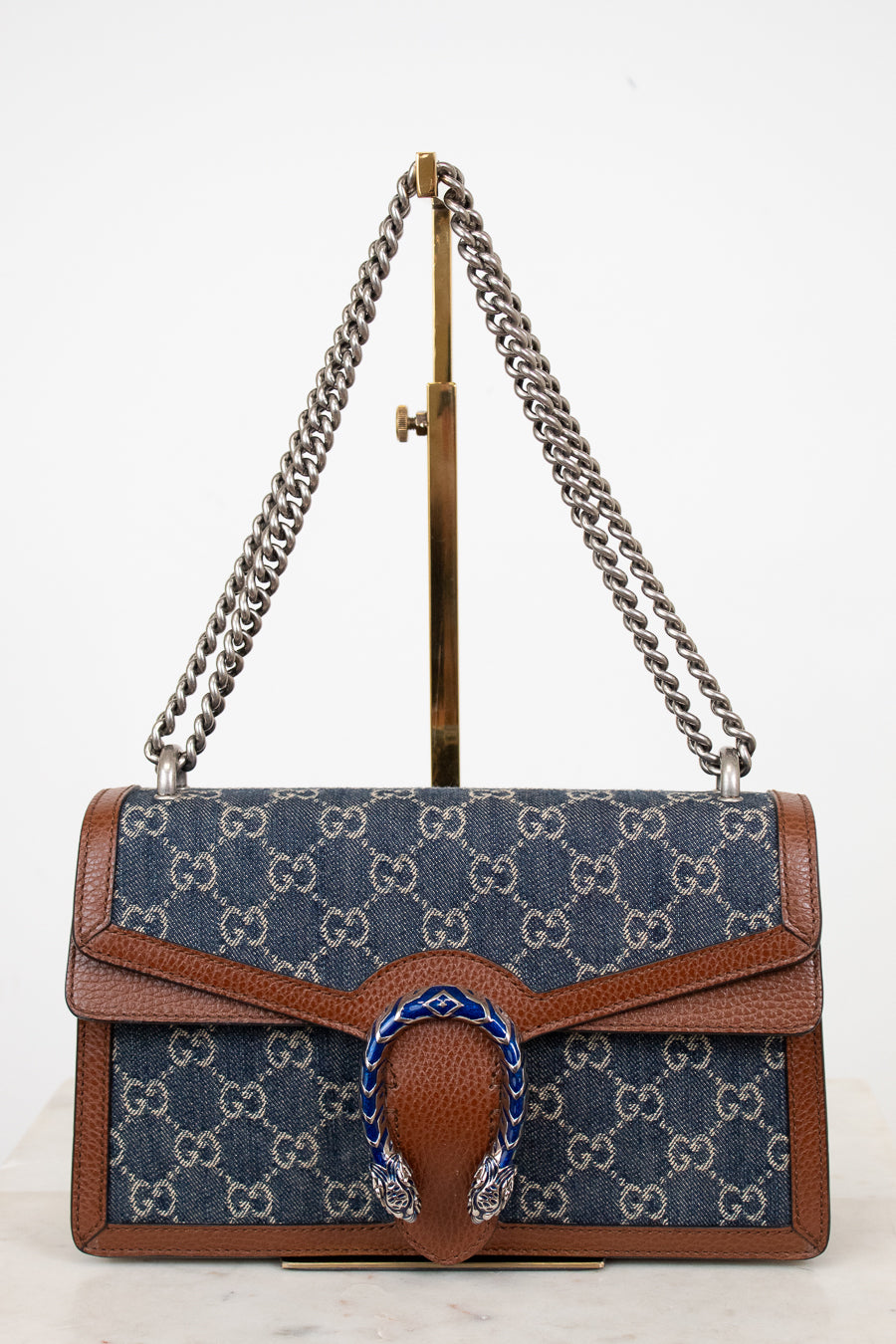Designer handbag with silver chain strap on a stand against a white background